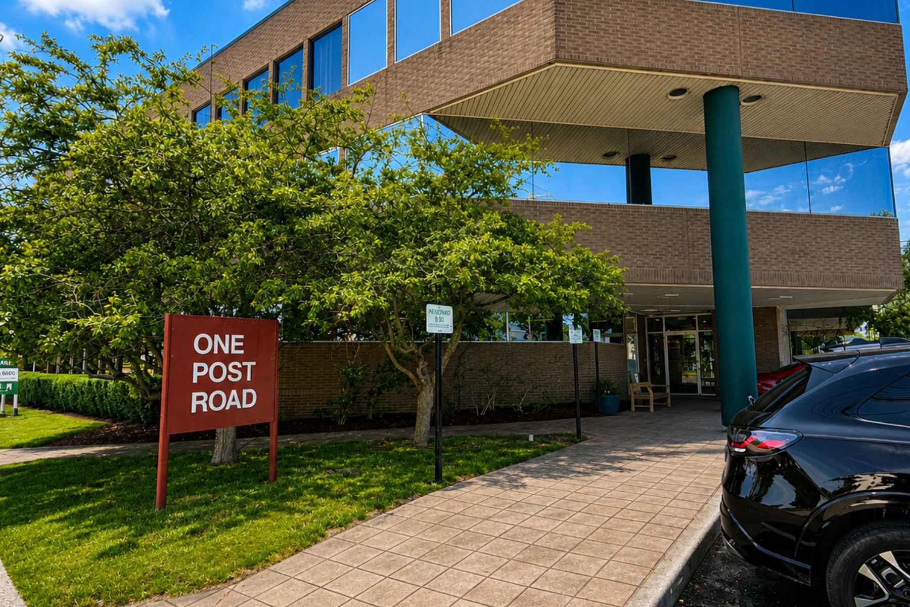 Entrance to 30,300 SF Waterfront Office Building Exterior street-level entrance of the One Post Road commercial office building in Fairfield, Connecticut, featuring a red monument sign and tree-lined driveway.