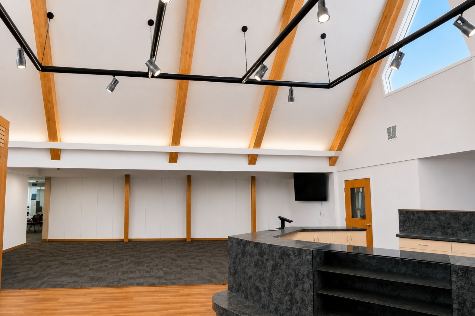Architectural Timber Framing and Soaring Vaulted Ceilings Provide a Premium Modern Aesthetic for a Flagship Location Open-concept commercial showroom featuring soaring vaulted ceilings, architectural timber framing, and modern track lighting.